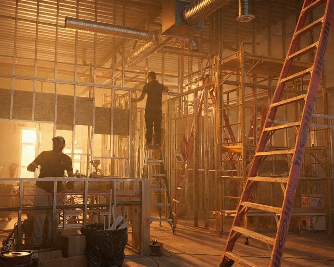 A Luminova crew framing interior partitions during a commercial fit-out, with overhead ductwork, scaffolding and ladders in place