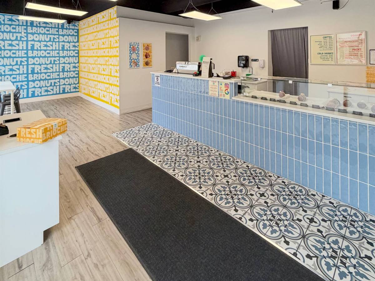 Completed fit-out at Pate Sucree: blue and yellow typographic murals reading FRESH, BRIOCHE and DONUTS, a blue tile service counter with pastry display case, and patterned encaustic floor tile