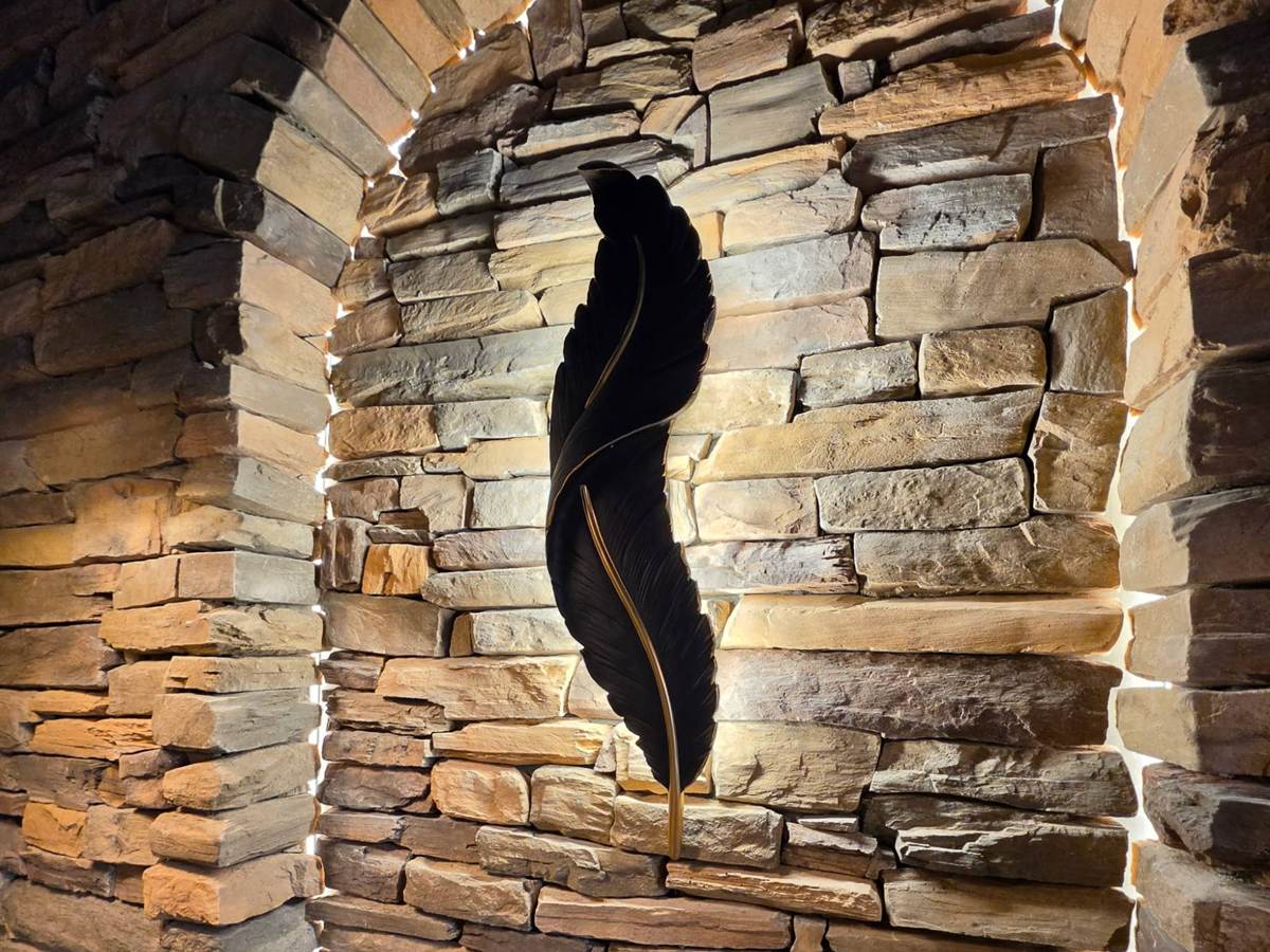 Backlit dry-stacked stone feature wall at Sardar Ji Bar and Grill: an arched alcove lit from behind each course, with a large black and gold feather sculpture mounted at its centre